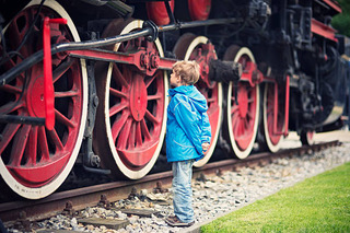 Little boy and the steam locomotive Little boy admiring a giant steam locomotive. The boy aged 5 is examining details of the red steel wheel that is bigger than the boy. The boy is wearing green jacket and jeans. steam train stock pictures, royalty-free photos & images